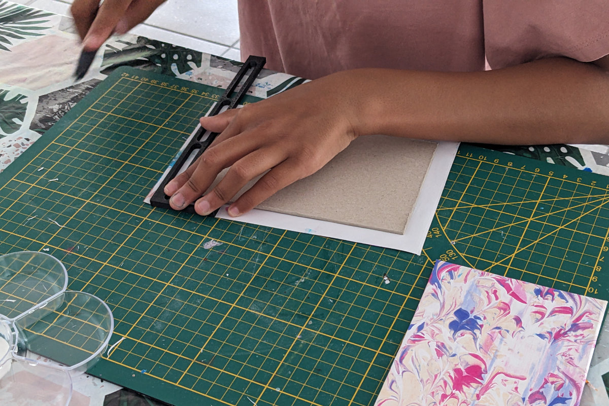 Mains d'enfant découpant les rembords de sa couverture à l'aide d'un cutter et d'une règle en L