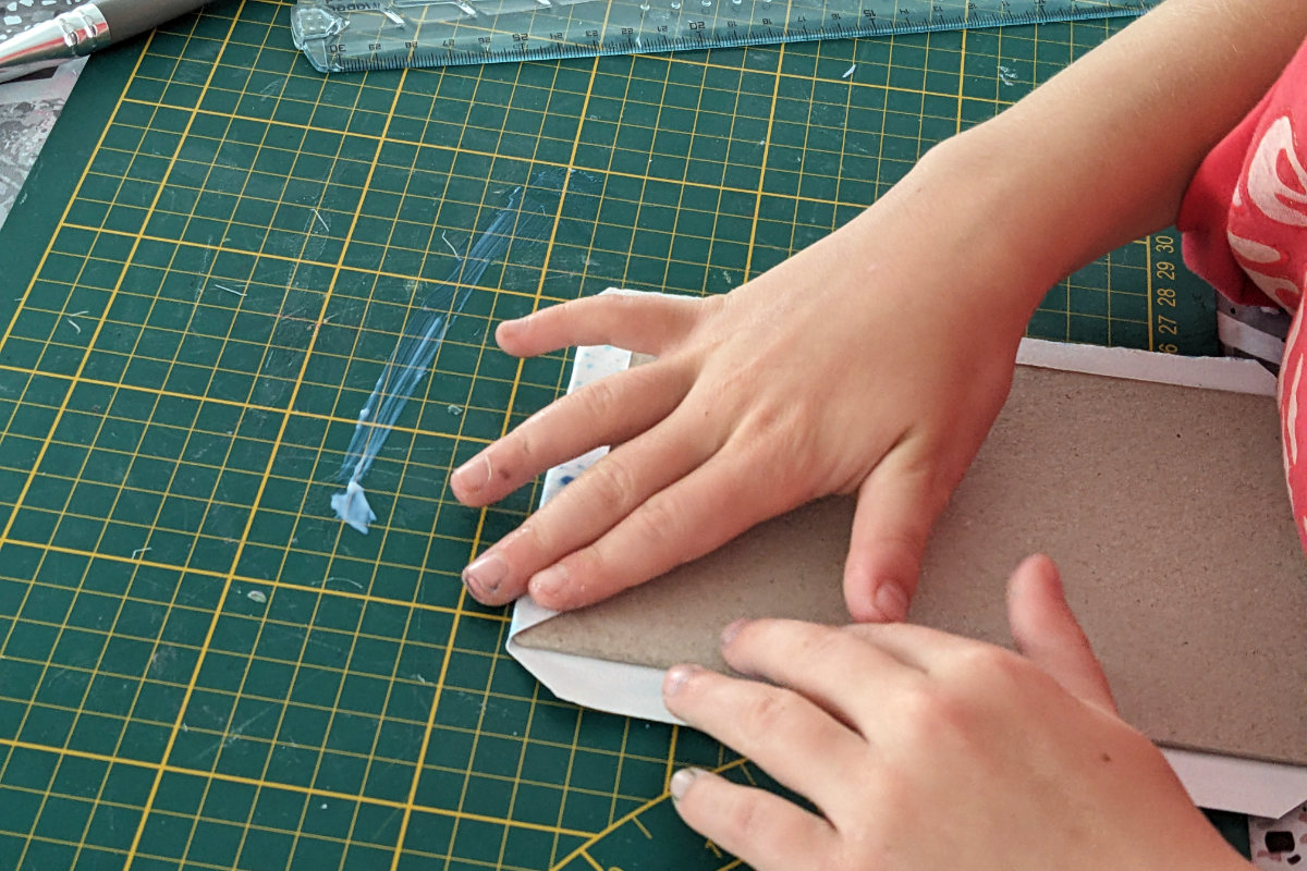 Mains d'enfant repliant un rembord sur le carton de sa couverture